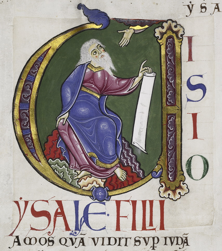 A white-bearded man dressed in bright red and blue robes holds an unfurled scroll while sitting on a colorful rock; he looks upward to a disembodied hand. The scene is enclosed in a large initial shaped like a modern lowercase u, though the multicolored capitals to the right of 'ISIO' makes clear the initial should be read as a 'V'. The text below continues in large colored capitals: 'YSAIE FILII' and in regular-sized, regular-inked capitals below that: 'AMOS QVA VIDIT SUP(with stroke through descender) IVDA(with macron).